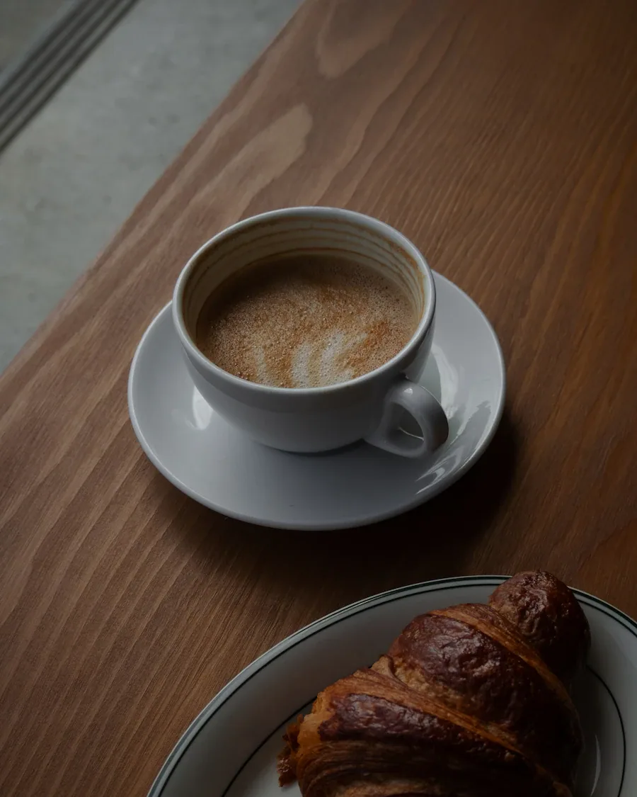 Un croissant junto a una taza de café sobre una mesa de madera